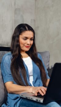 Smiling  brunette woman working by laptop while sitting at home.   - Image